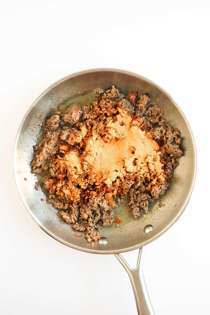 Ground beef cooking in a skillet with taco seasoning powder sprinkled on top, perfect for assembling Tochos or loading onto a Sheet Pan for an easy meal.