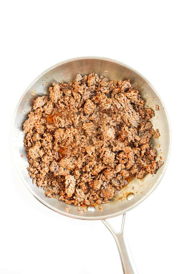 A metal skillet filled with cooked ground beef, seasoned and browned, perfect for adding to nachos or sheet pan tochos, on a white background.