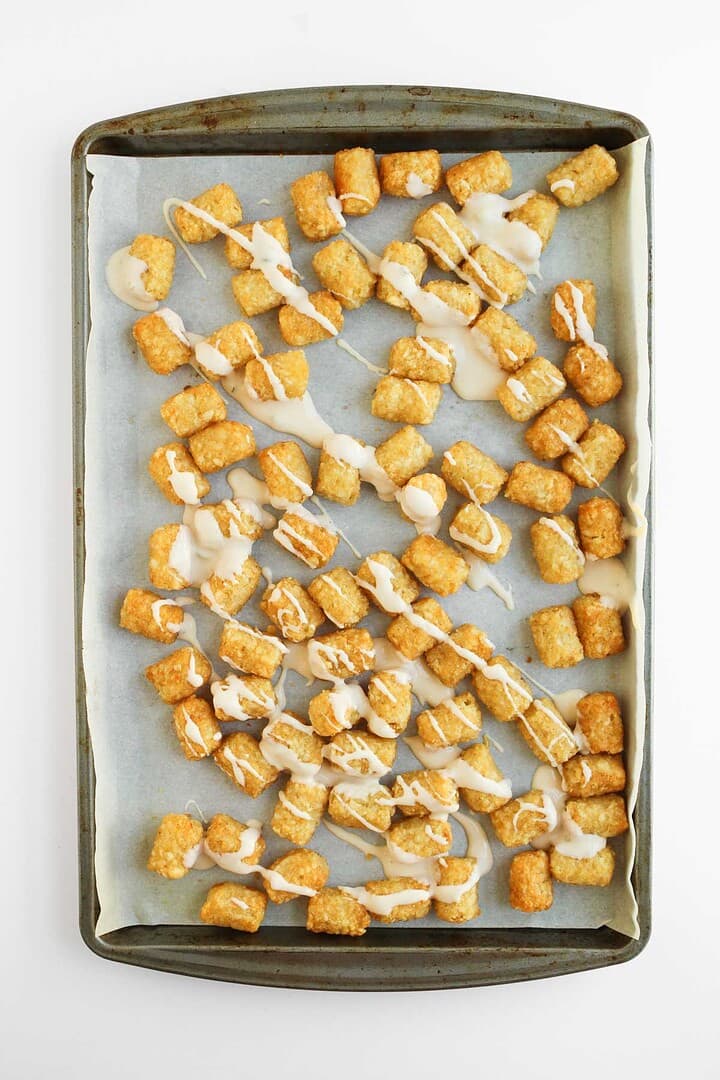 A sheet pan of tater tots, also known as tochos, drizzled with melted cheese and lined with parchment paper.