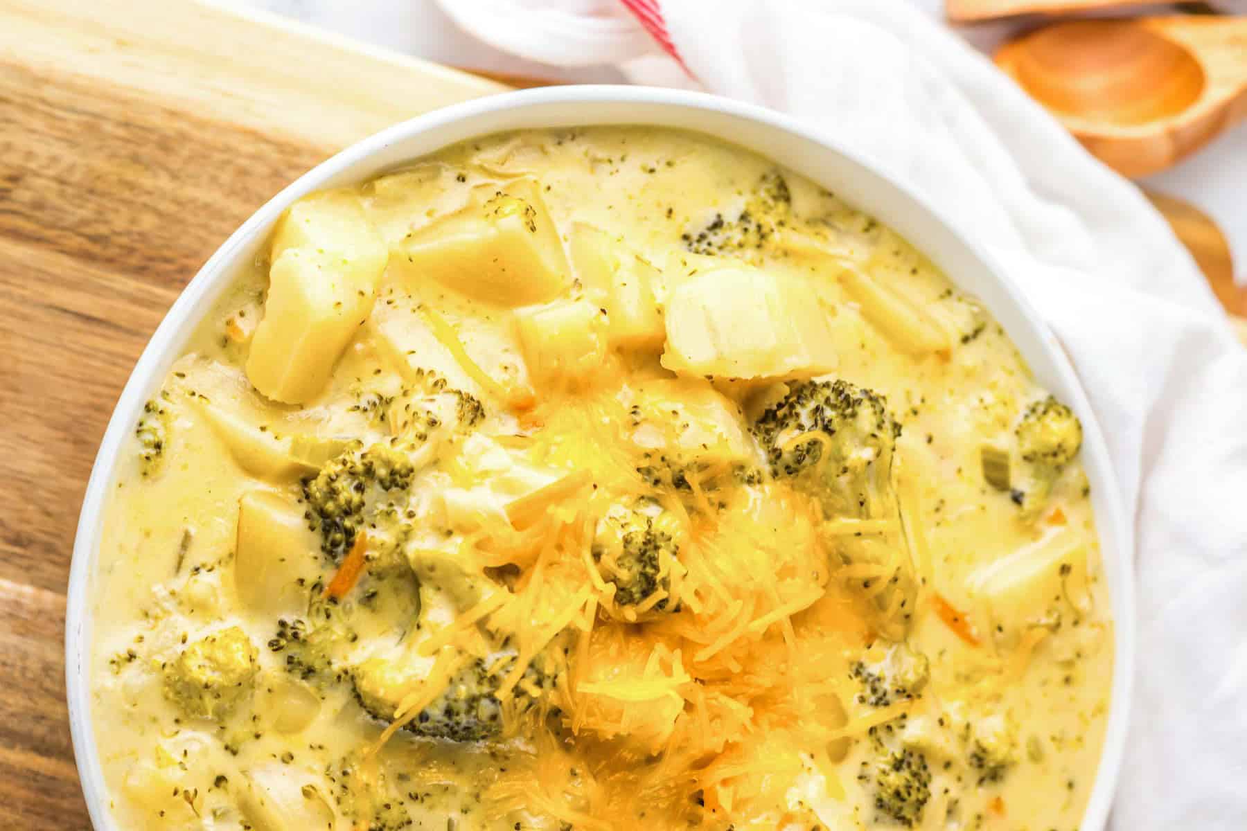 Bowl of creamy cheesy broccoli soup topped with shredded cheese, placed on a wooden board—perfect for a cozy slow cooker soup night.