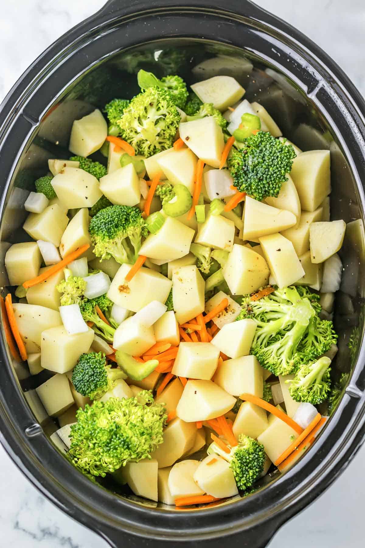 Chopped broccoli, potatoes, carrots, celery, and onions in a slow cooker—perfect for making a creamy cheesy broccoli potato soup.