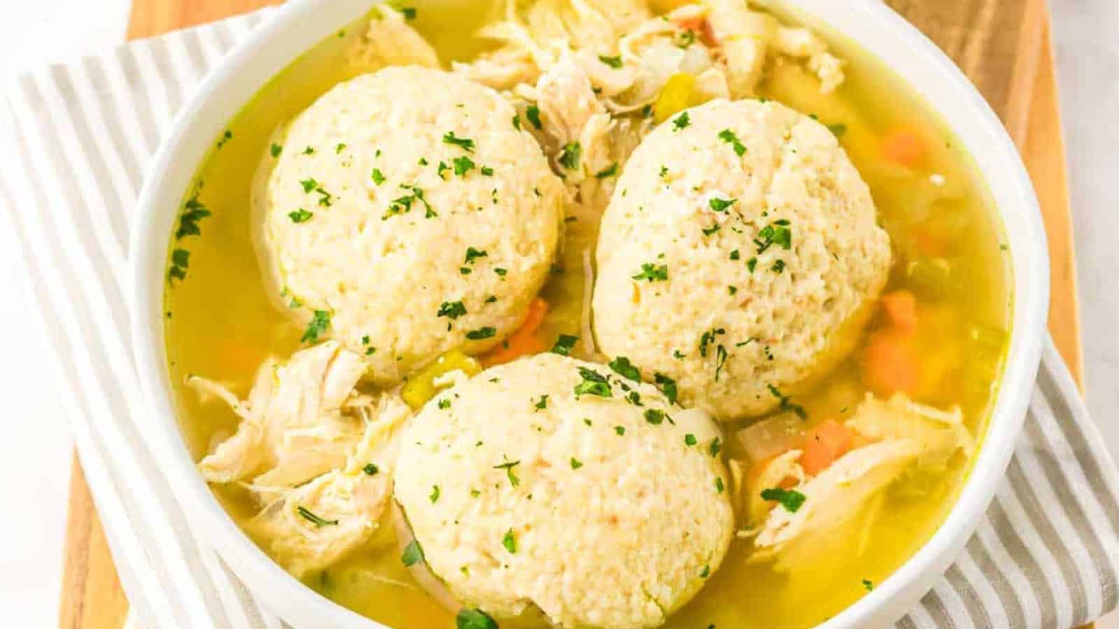 Bowl of chicken and dumplings soup with shredded chicken, vegetables, and three large dumplings, garnished with herbs.