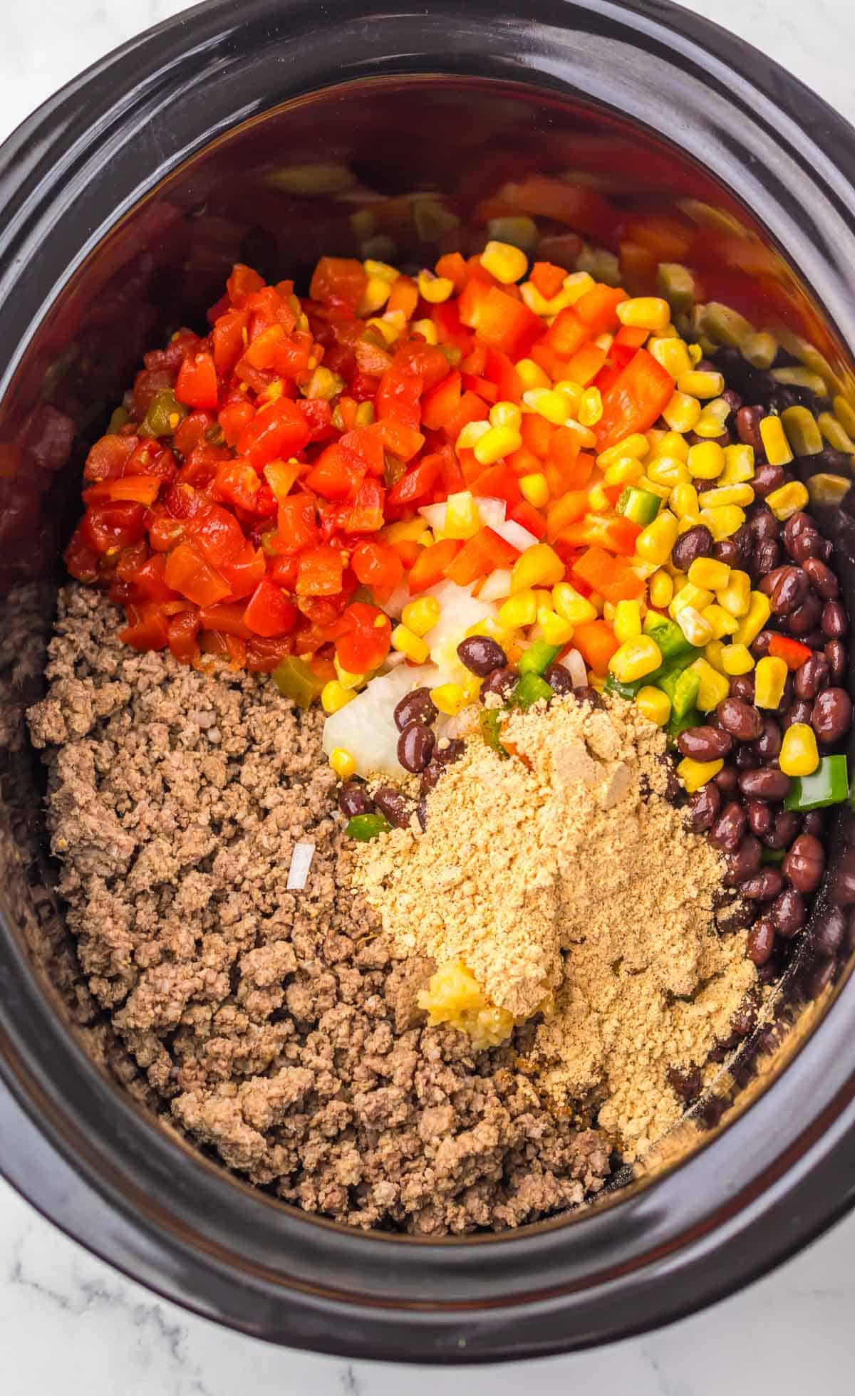 Nacho Soup made with ground beef, beans, corn, diced tomatoes, onions, and seasoning in a slow cooker, seen from above.