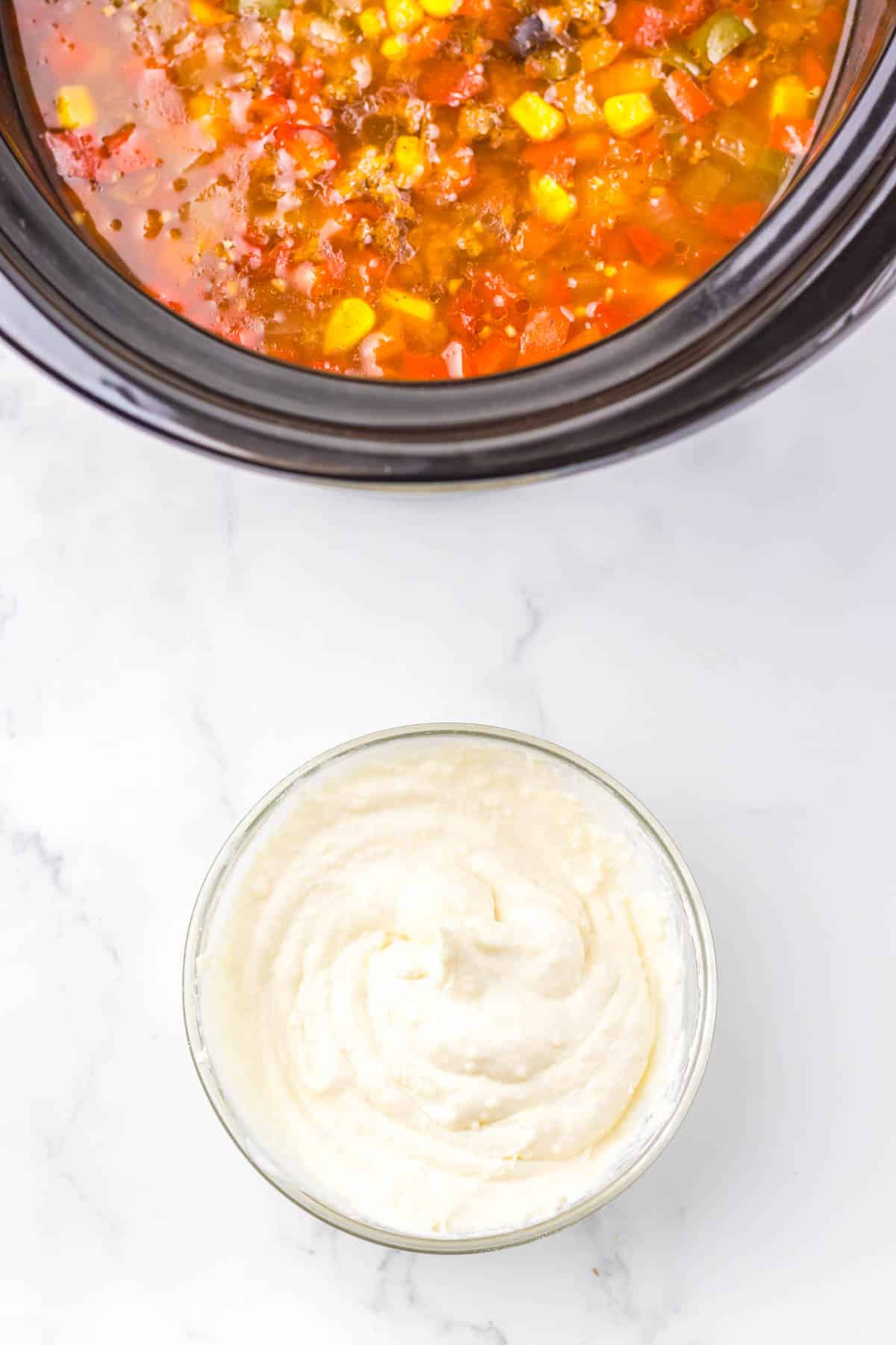 A bowl of mashed potatoes sits beside a slow cooker filled with a colorful vegetable and meat stew, perfect for trying a new recipe or serving alongside your favorite nacho soup.