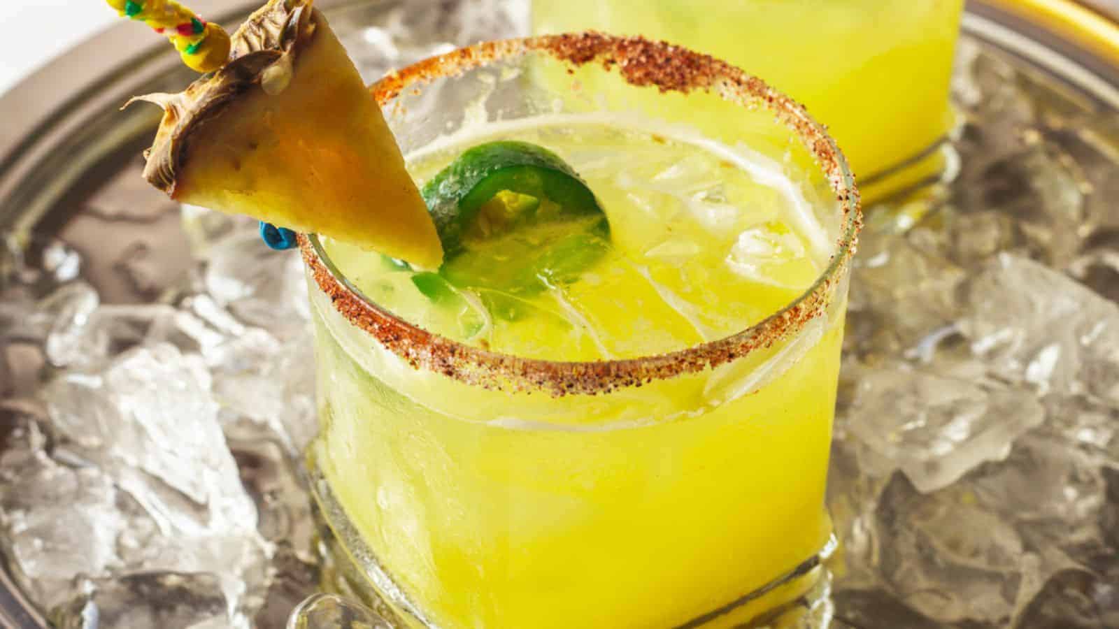 Yellow cocktail with a chili rim, ice, jalape&ntilde;o slices, and a pineapple wedge, served on an ice-filled tray&mdash;bursting with bold flavor for your next fiesta.