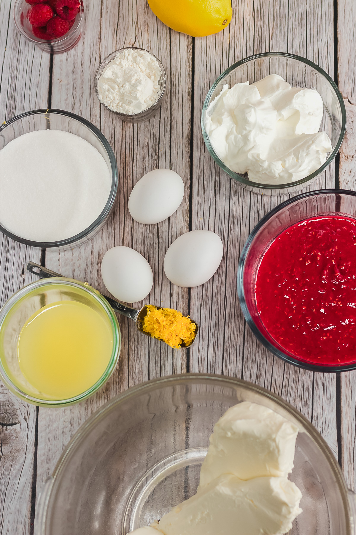 Baking ingredients on a wooden table: eggs, sugar, lemon, raspberries, cream cheese, juice, and zest—everything you need for a delicious Raspberry Lemon Cheesecake recipe. Perfect for making in your Instant Pot!.