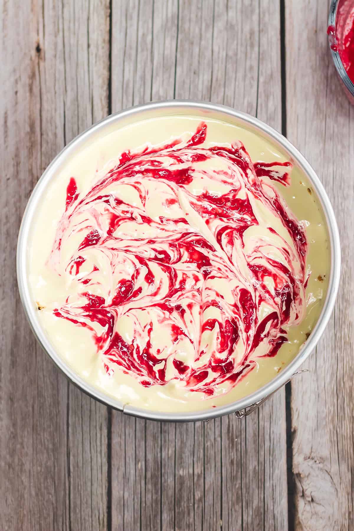 A Raspberry Lemon Cheesecake in a pan with a red and white swirled pattern on top, sitting on a rustic wooden surface—perfect for trying as your next Instant Pot recipe.