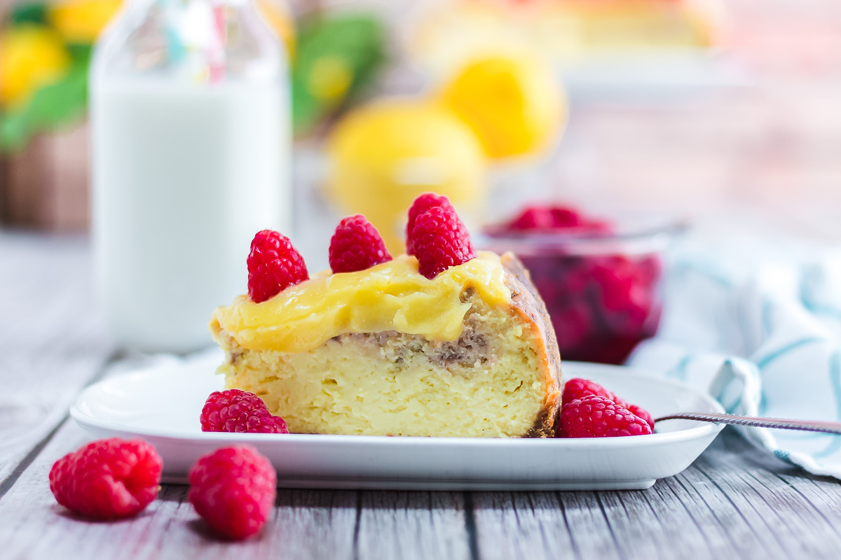 A slice of Raspberry Lemon Cheesecake topped with raspberries sits on a plate, accompanied by a glass of milk and more fresh berries—an irresistible treat you can easily make with this Instant Pot recipe.