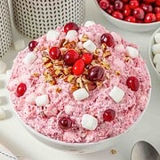 A bowl of pink cranberry fluff salad topped with cranberries, chopped pecans, and mini marshmallows.