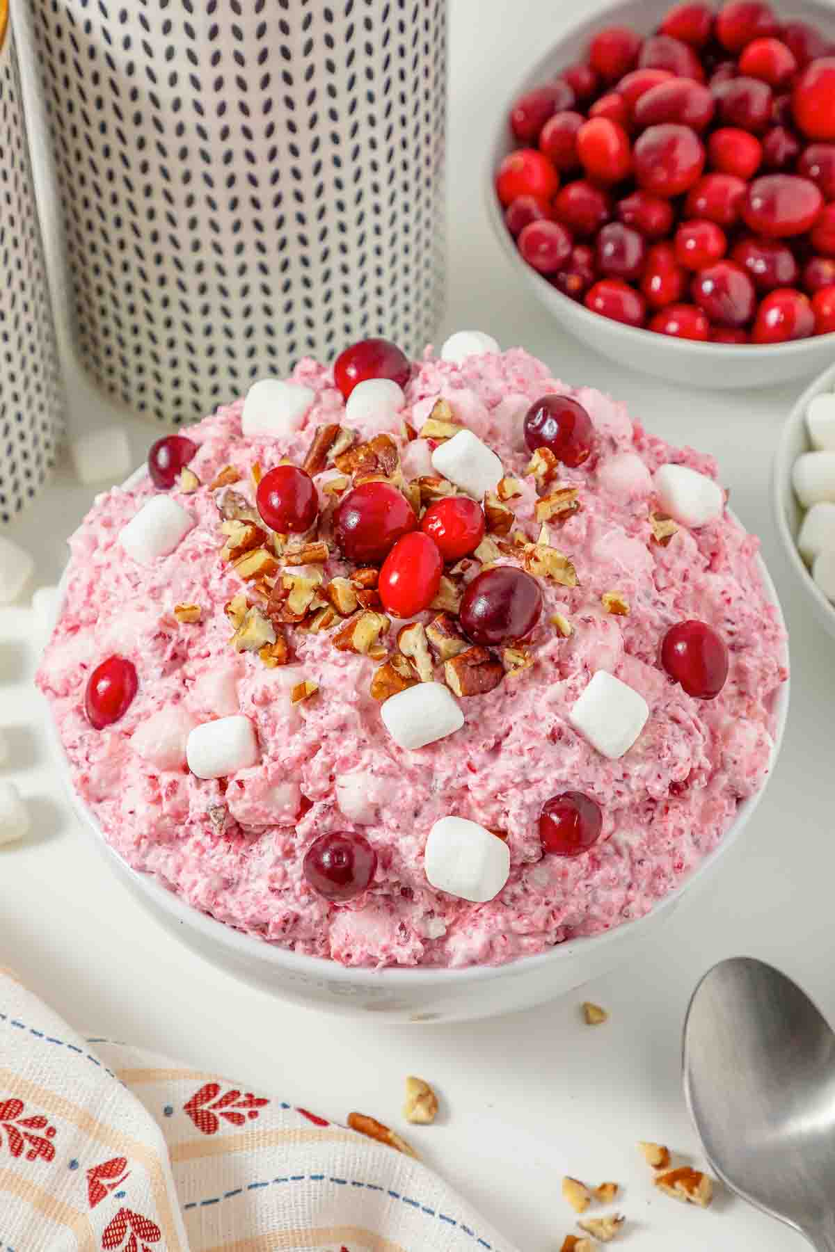 A bowl of pink cranberry fluff salad topped with cranberries, chopped pecans, and mini marshmallows.