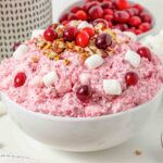 A bowl of pink cranberry salad topped with cranberries, pecans, and mini marshmallows.