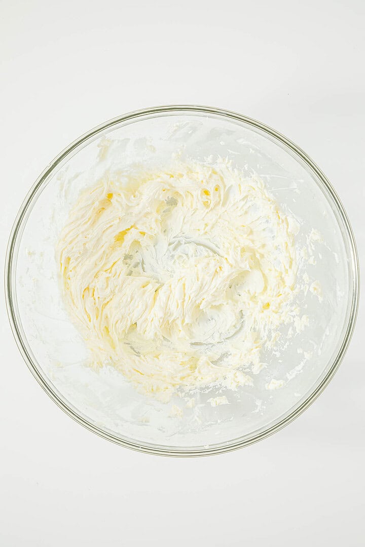 Clear glass bowl with fluffy, whipped cream or frosting mixture against a white background.