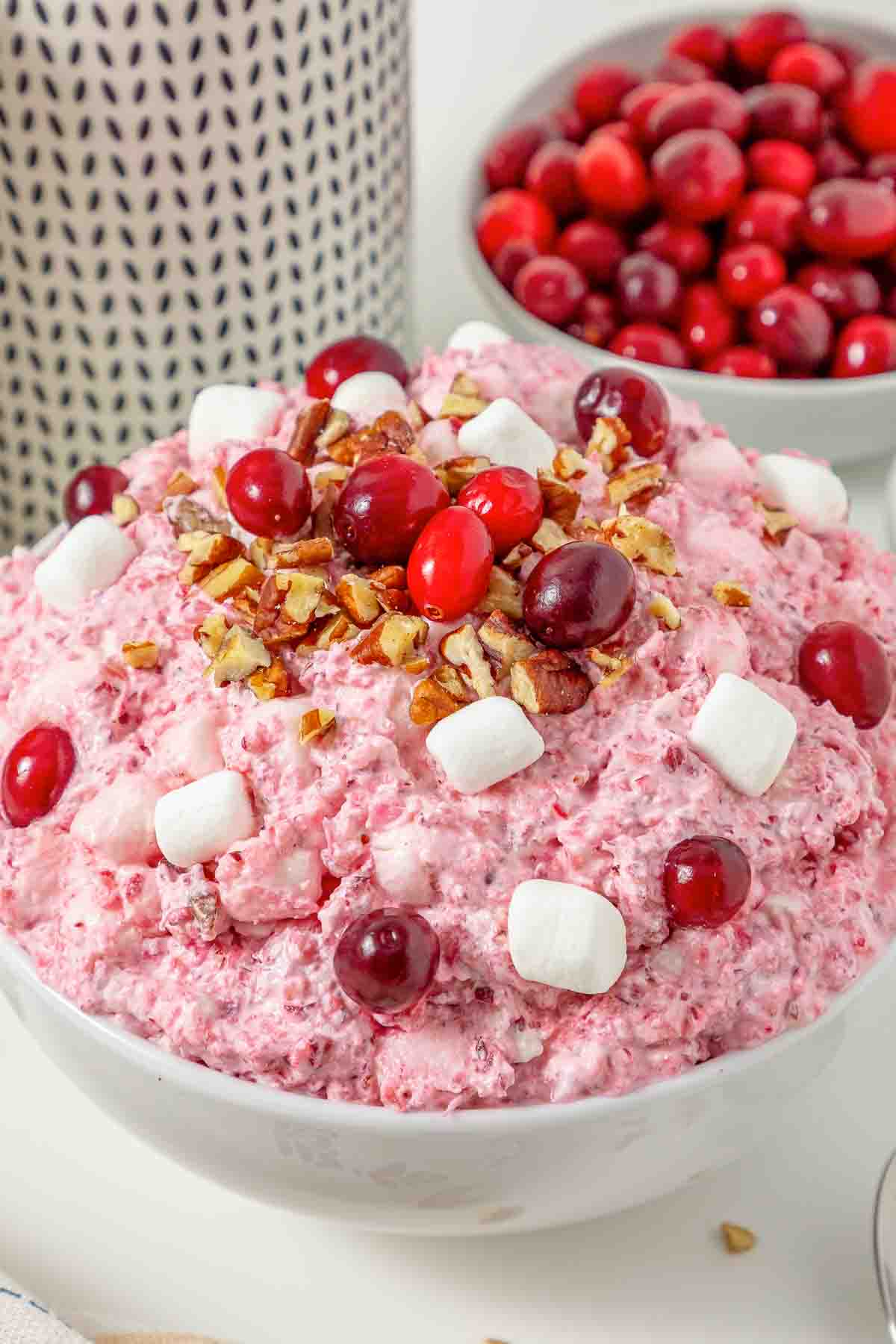 A bowl of pink Cranberry Fluff Salad topped with cranberries, marshmallows, and chopped pecans.