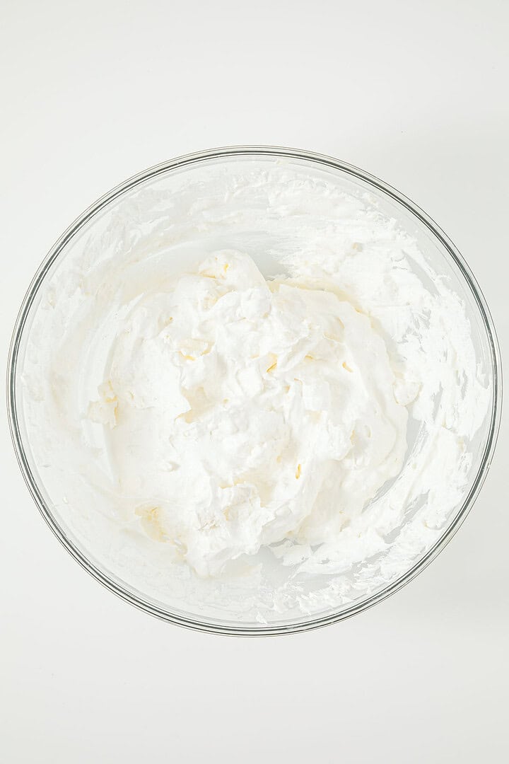 A glass bowl filled with fluffy whipped cream on a white surface.