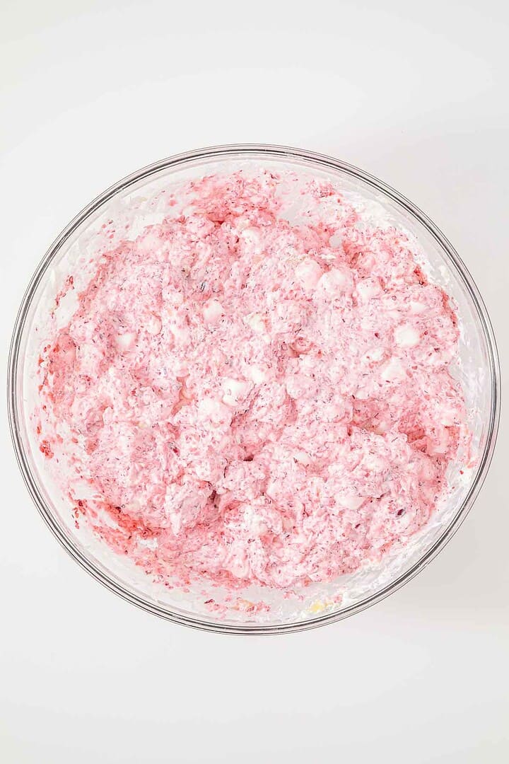 A glass bowl filled with a pink, fluffy dessert mixture containing small white marshmallows.
