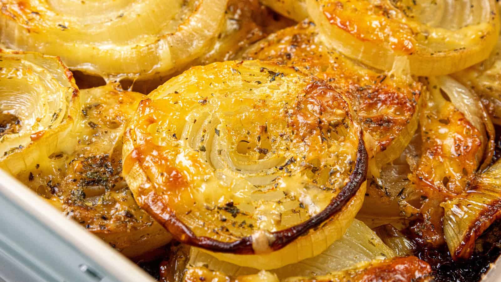 Close-up of roasted onion slices, golden and caramelized, sprinkled with herbs and seasoning.