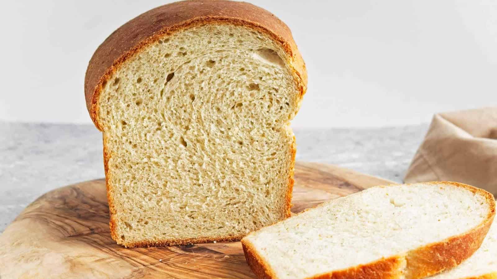 A loaf of sliced white bread on a wooden cutting board with a beige napkin in the background.
