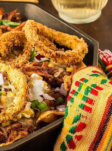 A skillet of nachos topped with pulled meat, onion rings, jalapeños, chopped onions, and melted cheese—perfect Cinco de Mayo finger foods.