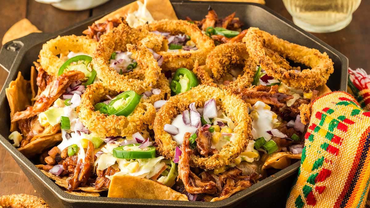 A skillet of nachos topped with pulled meat, onion rings, jalape&ntilde;os, chopped onions, and melted cheese&mdash;perfect Cinco de Mayo finger foods.