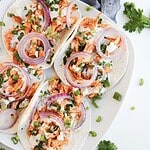 Four easy chicken tacos on a white plate, topped with red onion, green onions, and cilantro—perfect for those craving Buffalo chicken tacos with a fresh twist.