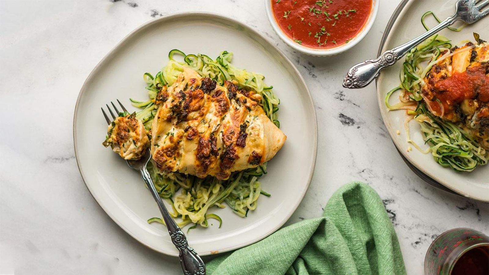Chicken breast with herbs on spiralized zucchini noodles, served with tomato sauce on the side.