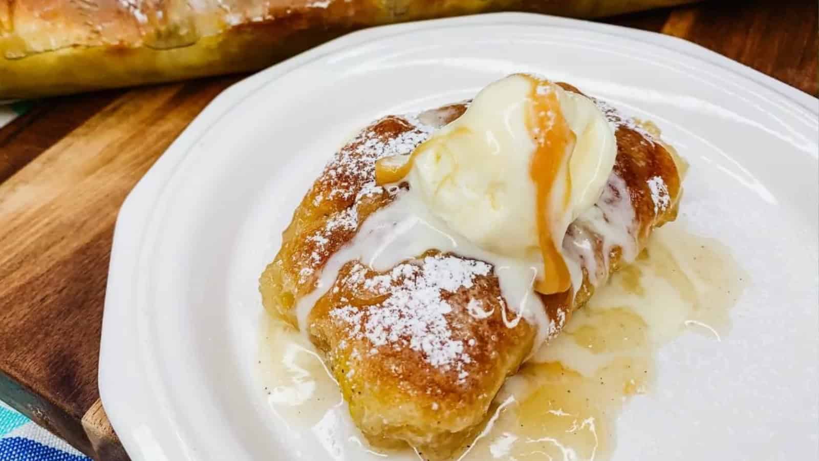 A golden pastry inspired by vintage recipes, topped with vanilla ice cream, caramel sauce, and powdered sugar on a white plate.