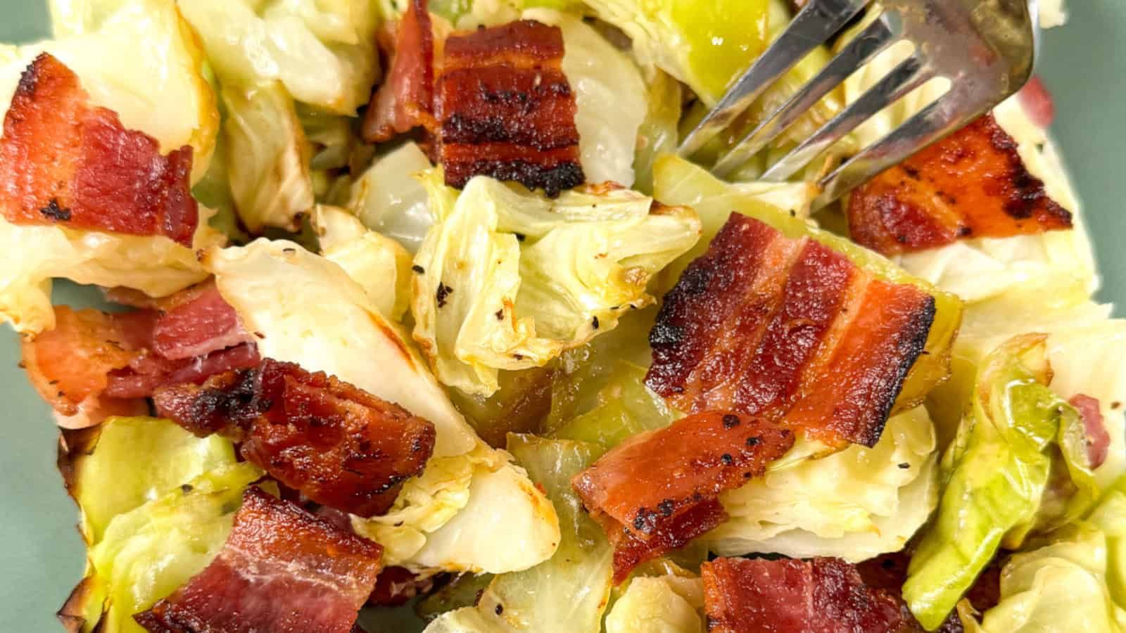 Chopped cooked cabbage and crispy bacon pieces with a fork on a plate.