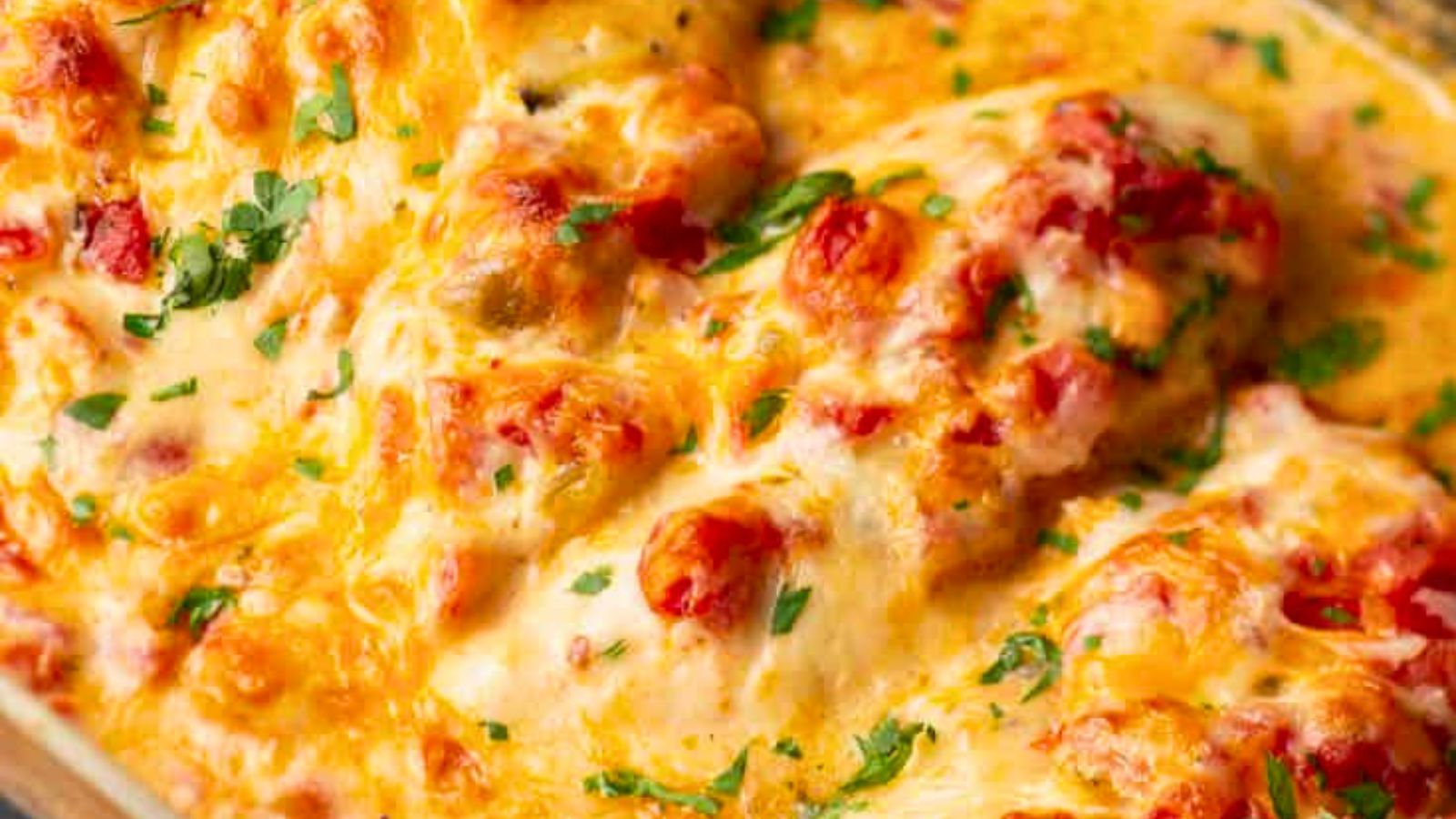 Baked chicken breasts in a creamy, cheesy sauce with tomatoes and chopped parsley on top.