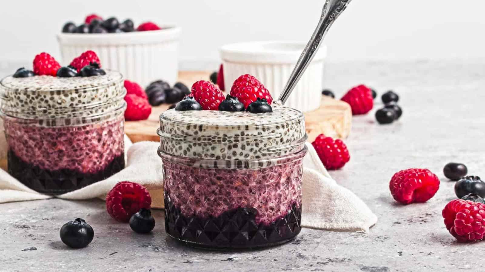 Layered chia pudding in jars topped with raspberries and blueberries, surrounded by scattered berries.