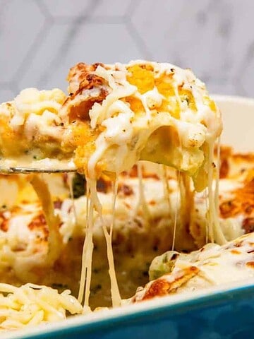 A fork lifts a cheesy, baked casserole with melted cheese stretching from a blue dish.