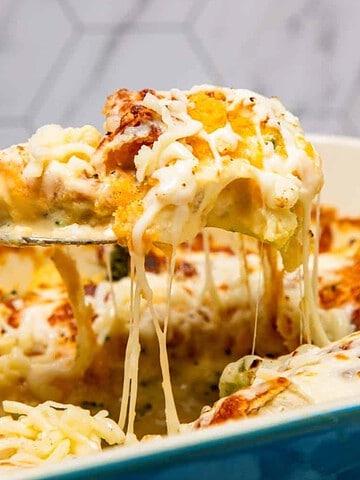 A cheesy casserole with browned top, being served from a blue dish with gooey, melted cheese stretching.