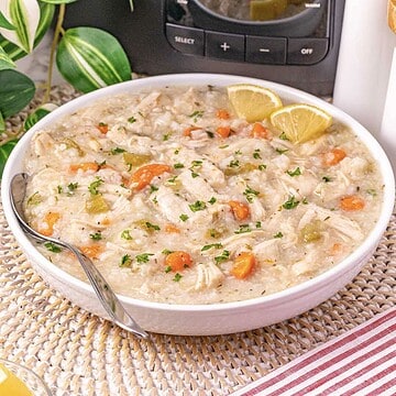 Bowl of creamy turkey and rice soup made with leftover turkey, carrots, celery, and parsley, garnished with lemon wedges.