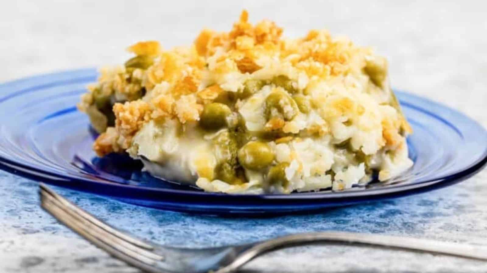 A serving of casserole with peas and a crumb topping on a blue plate, fork in front.