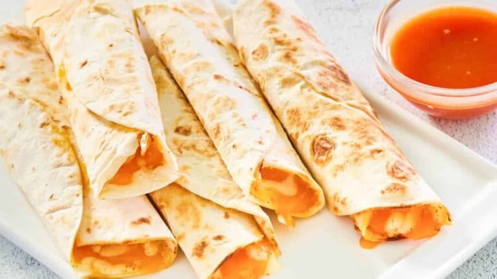 Five cheese-filled rolled tortillas on a white plate, with a small bowl of red sauce on the side.