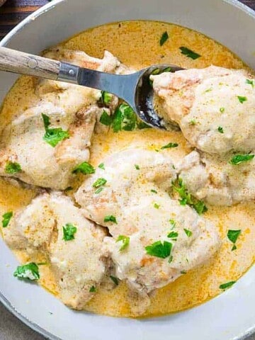 Chicken thighs in a creamy sauce garnished with parsley in a skillet, served with roasted baby potatoes.