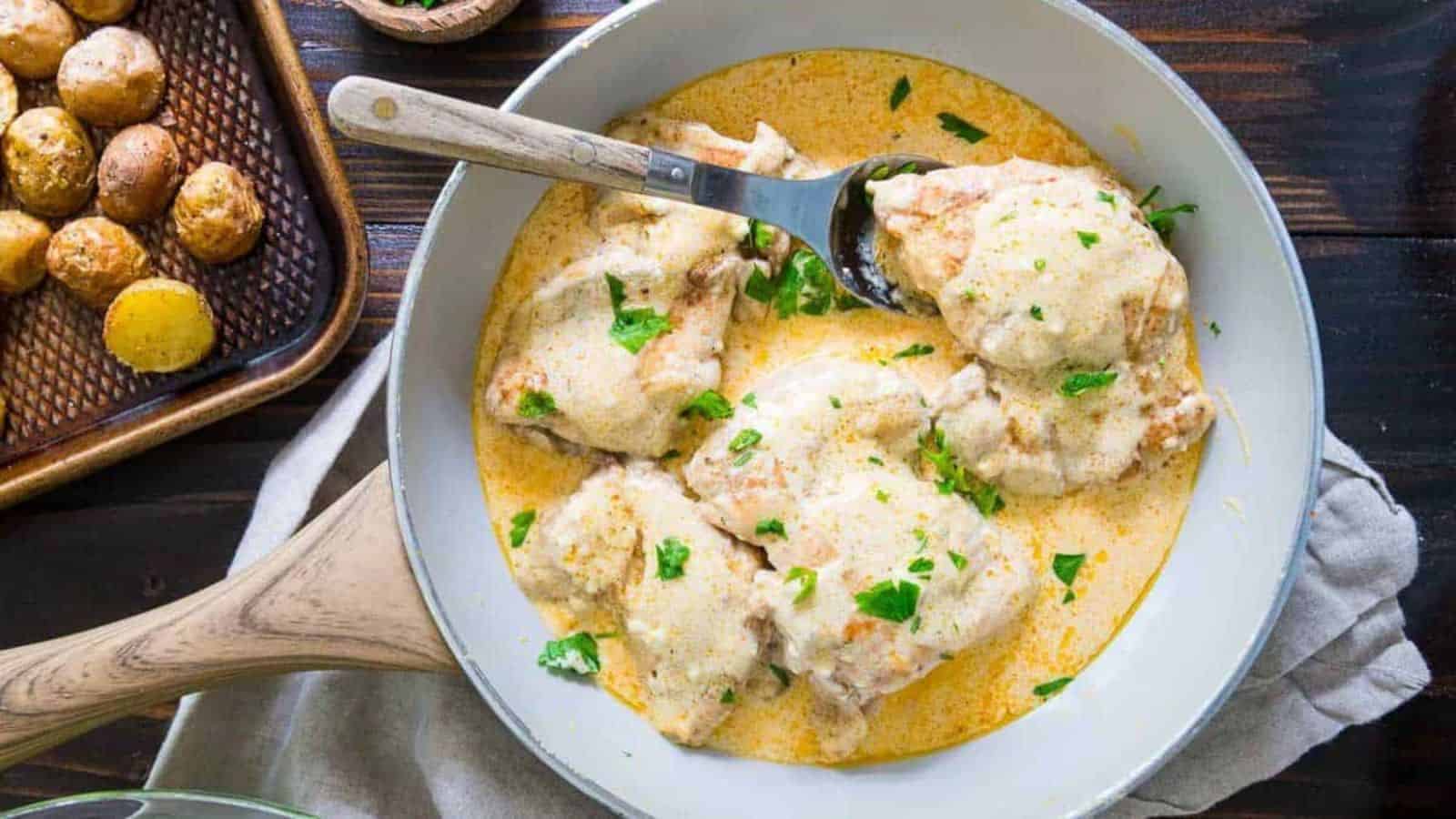 Chicken thighs in a creamy sauce garnished with parsley in a skillet, served with roasted baby potatoes.