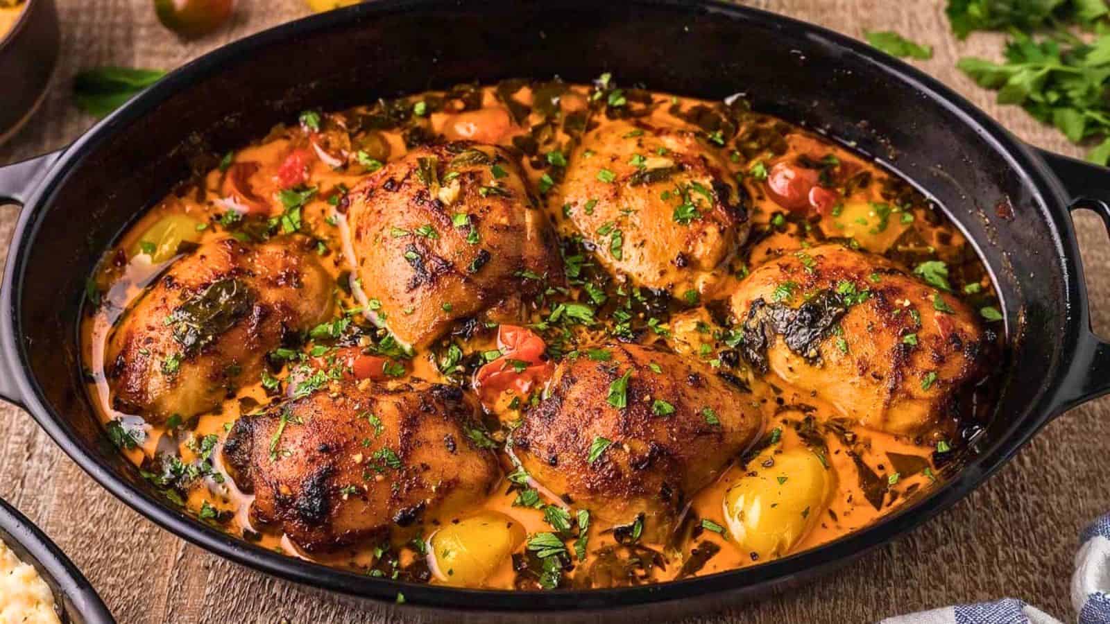 Roasted chicken thighs with herbs, tomatoes, and peppers in a black baking dish.