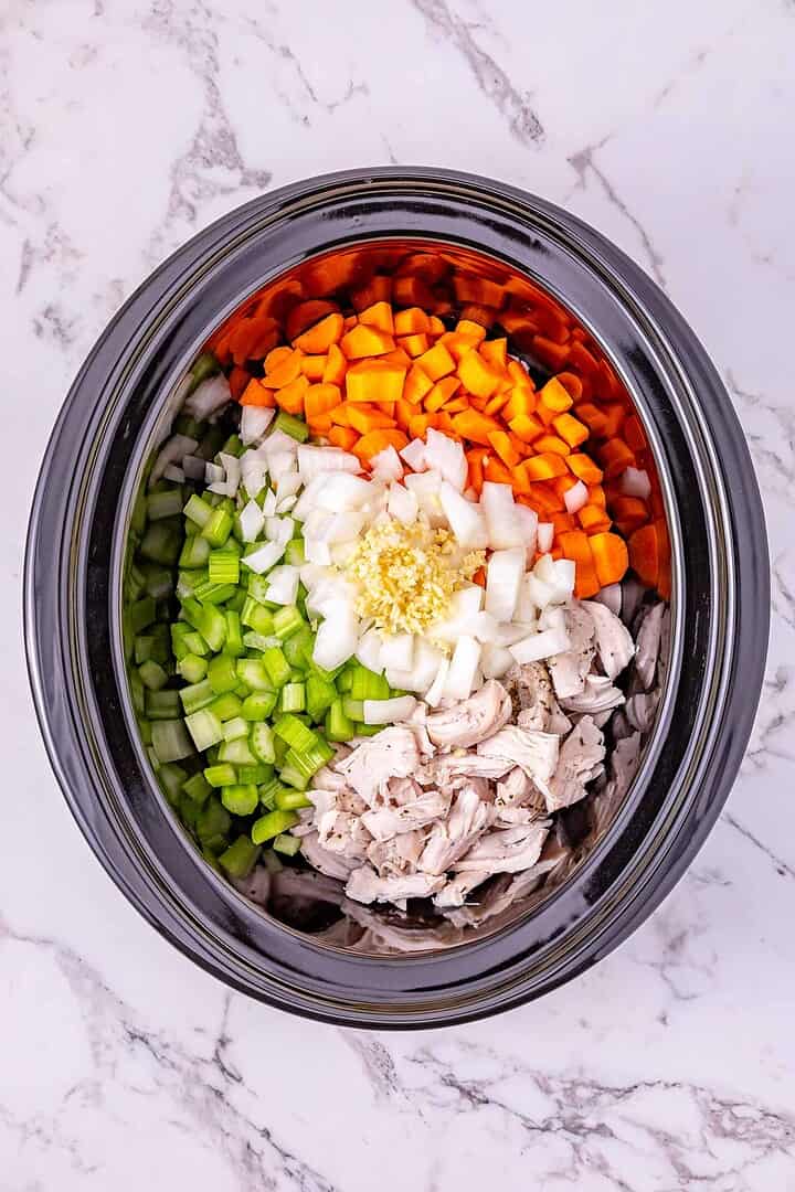 Overhead view of a slow cooker filled with chopped carrots, celery, onion, garlic, and shredded turkey for a hearty slow cooker turkey soup.