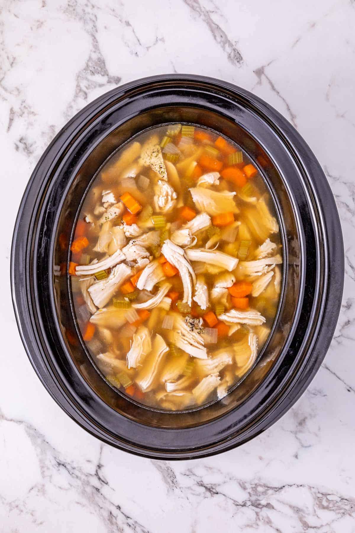 Leftover Turkey Rice Soup with carrots and celery in a black slow cooker on a marble countertop, viewed from above.