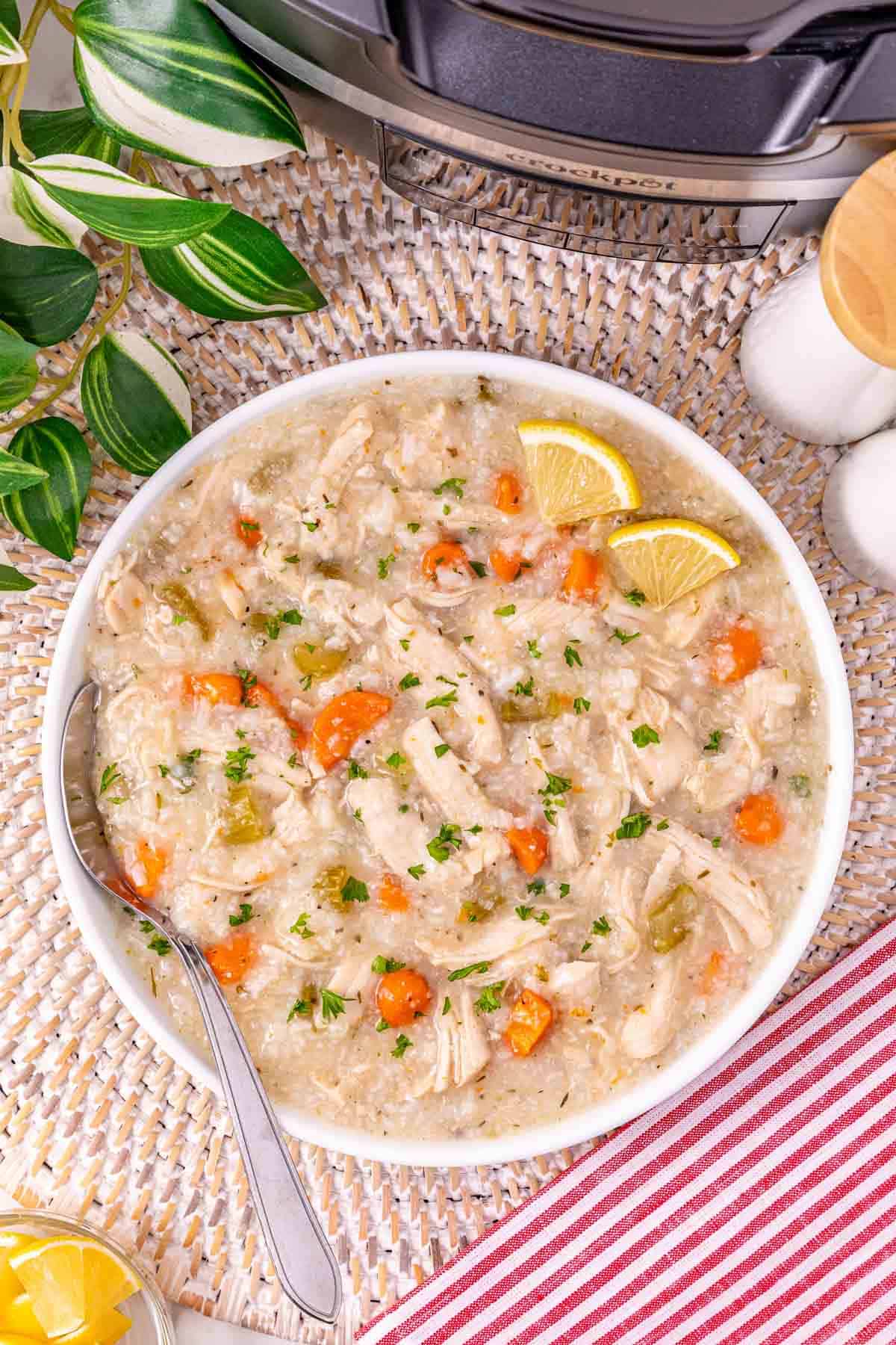 Bowl of turkey and rice soup made from leftover turkey, with carrots, topped with lemon slices and parsley, on a woven mat with a spoon.