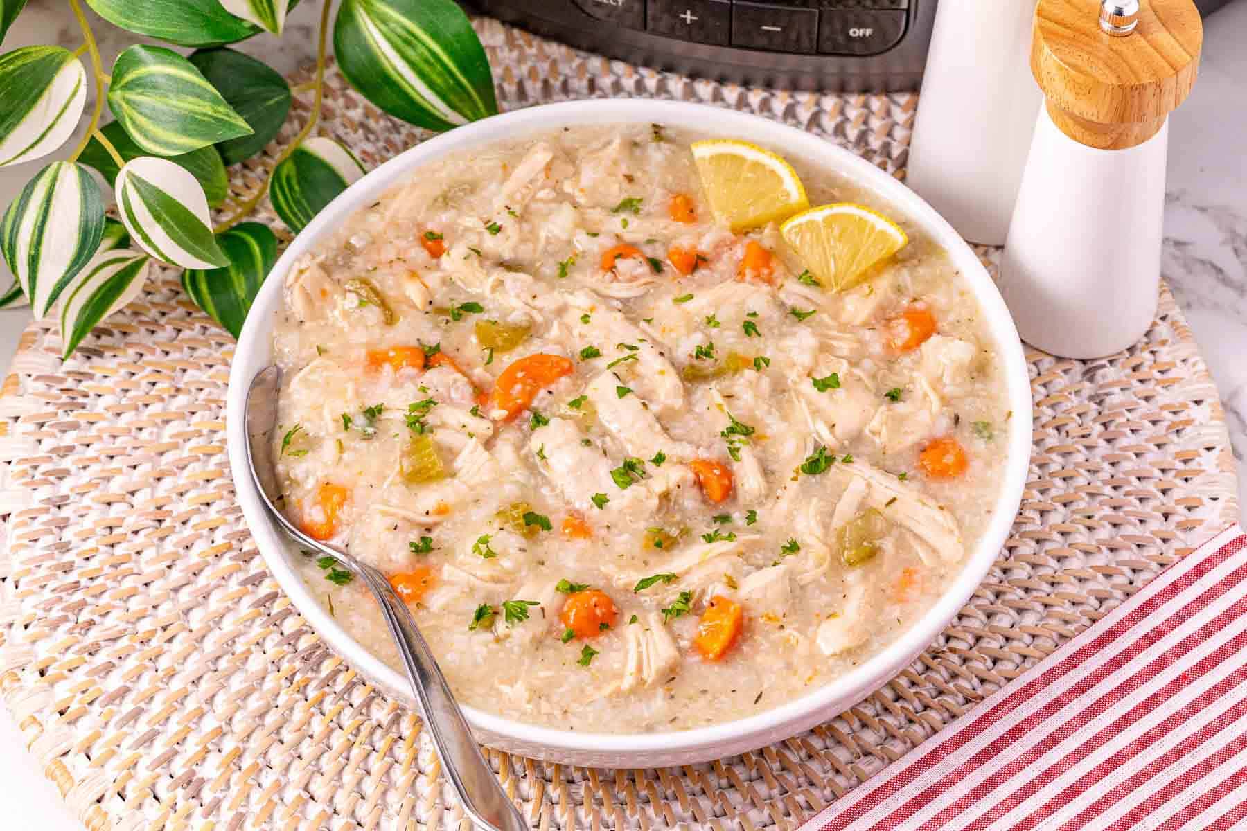 A bowl of turkey and rice soup with carrots and lemon wedges, garnished with parsley and a spoon—a comforting way to enjoy slow cooker turkey soup or use leftover turkey soup after the holidays.