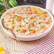 A bowl of creamy turkey and rice soup with carrots, garnished with parsley and lemon wedges, sits in front of a Crockpot—perfect for using up leftover turkey in your slow cooker.