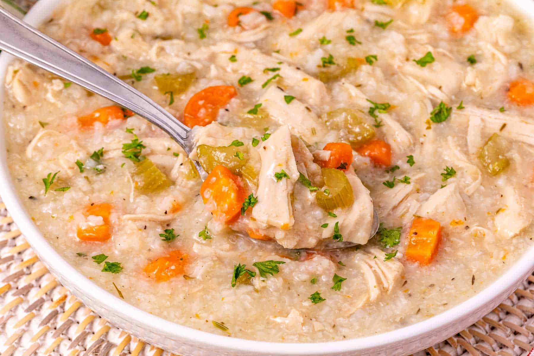 Bowl of slow cooker turkey soup with rice, carrots, celery, and parsley, with a spoon scooping some up.