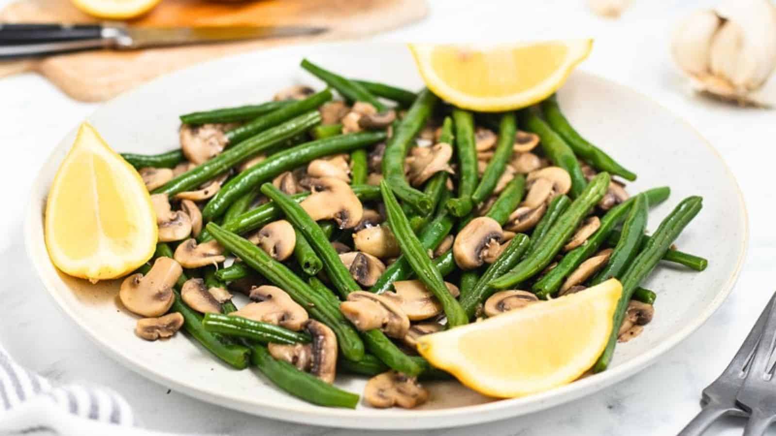 Sautéed green beans and mushrooms on a plate, garnished with lemon wedges.