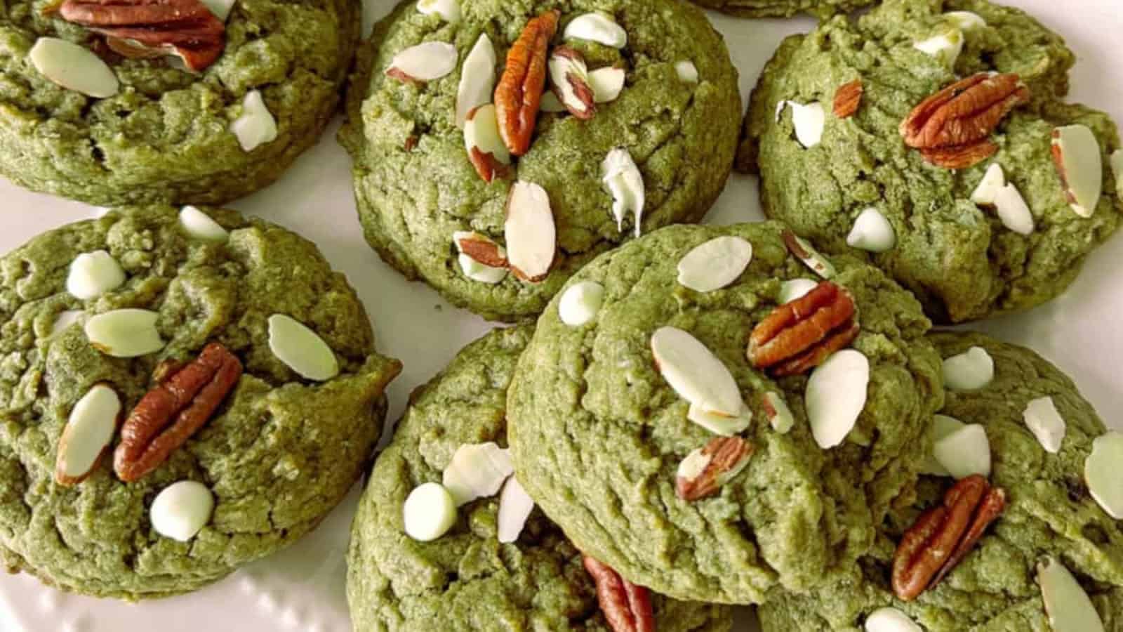 Green matcha cookies topped with white chocolate chips, pecans, and almond slices on a white plate.