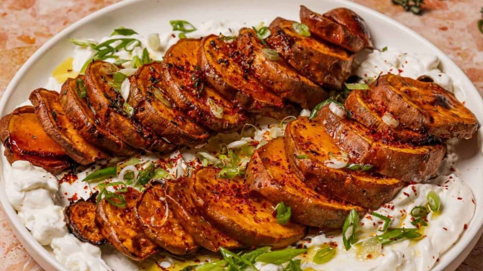 Sliced roasted sweet potatoes on a bed of creamy yogurt, garnished with green onions and spices.