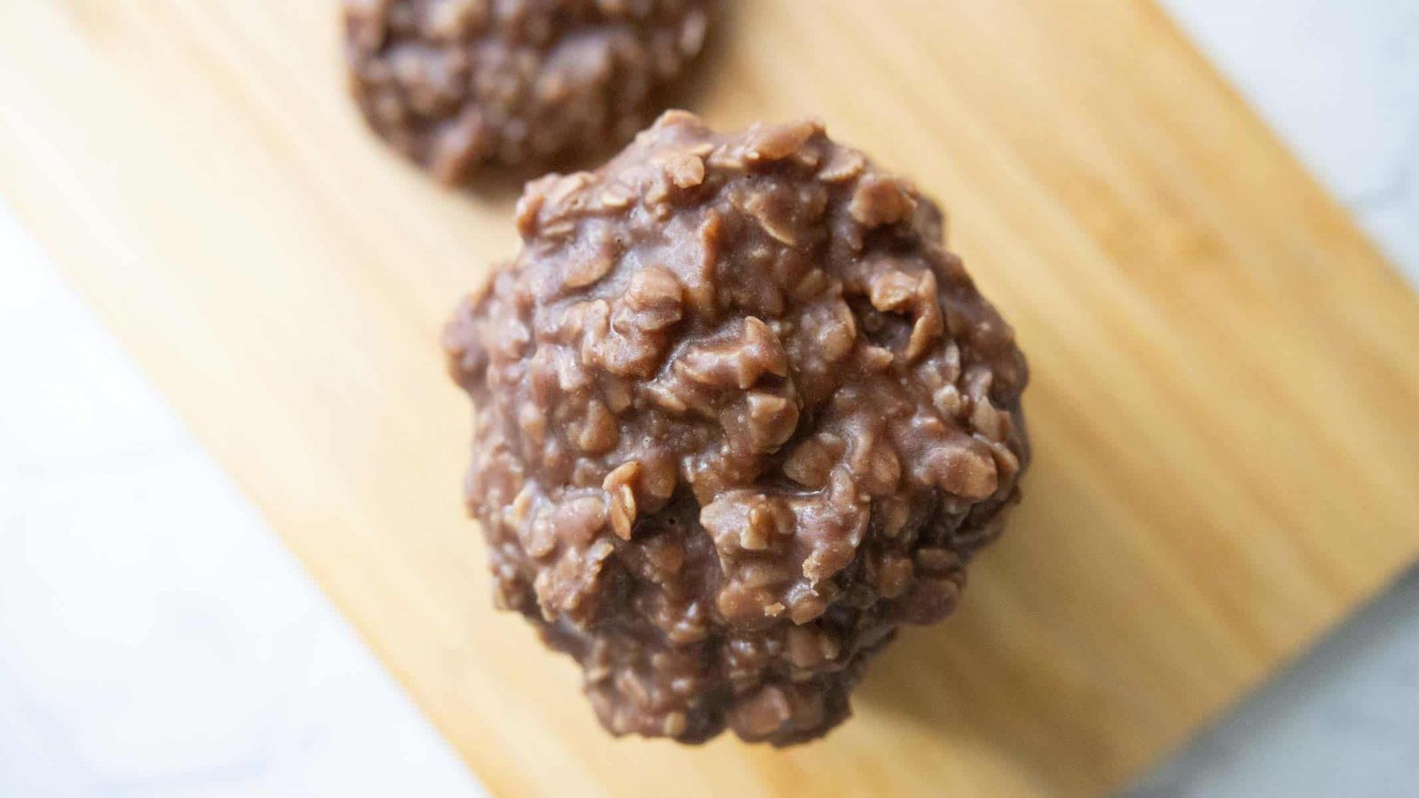A chocolate oatmeal no-bake cookie on a wooden board, with another cookie blurred in the background.
