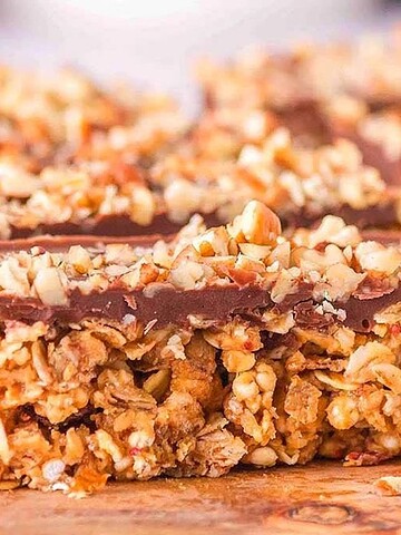 Granola bars topped with chocolate and chopped nuts, arranged on a wooden surface.