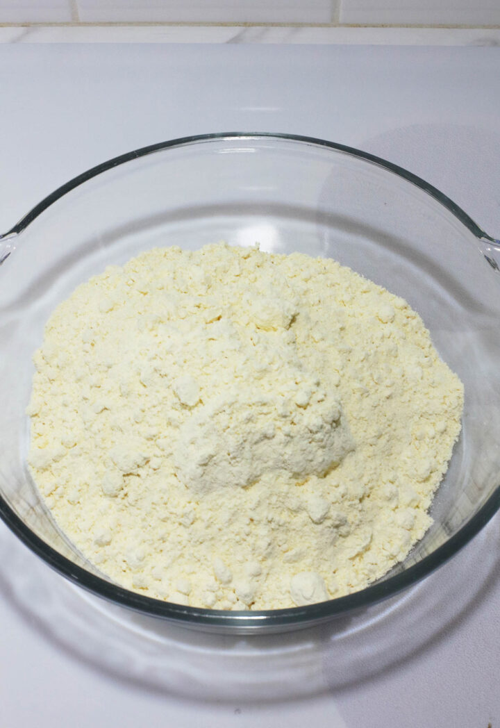 A glass bowl filled with a mound of yellowish flour sits on a white surface, perfect for crafting a no egg banana cream poke cake recipe.
