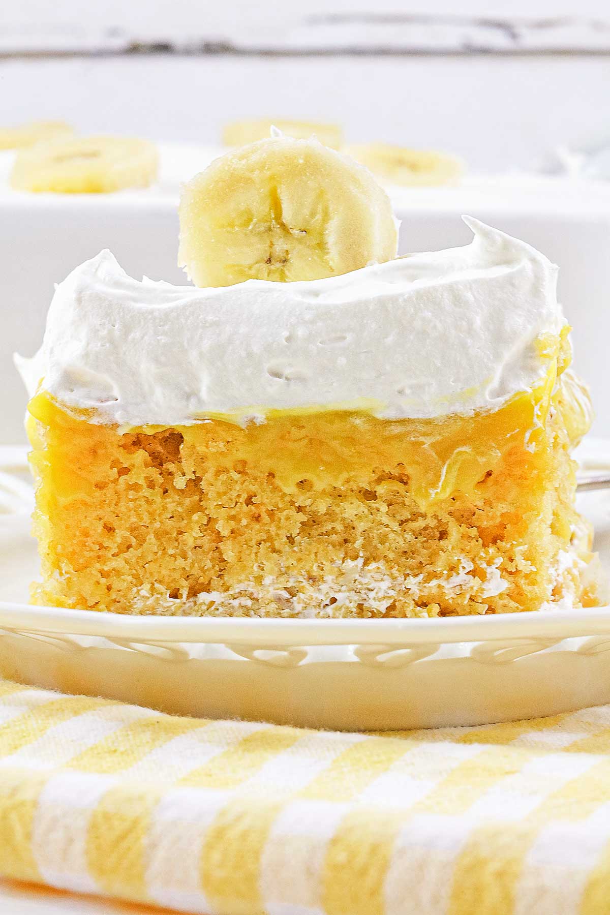 A slice of banana cream poke cake topped with whipped cream and a banana slice on a plate.